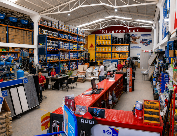 Asesor de Ferretería Al Día atendiendo a un cliente en sala de ventas, rodeado de herramientas y productos de construcción